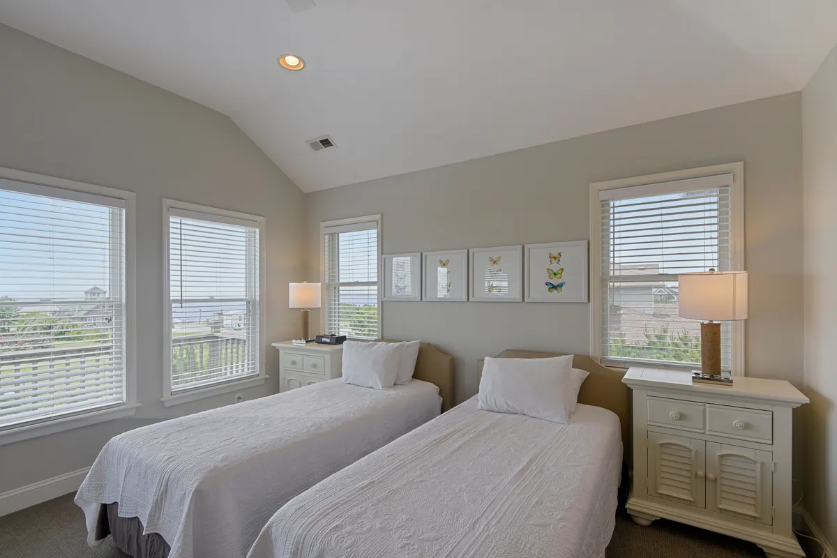 A peaceful twin bedroom featuring two inviting beds, whimsical butterfly artwork, and a pair of table lamps. The room is bathed in gentle daylight from the window, offering a cheerful yet restful environment ideal for families or friends.
