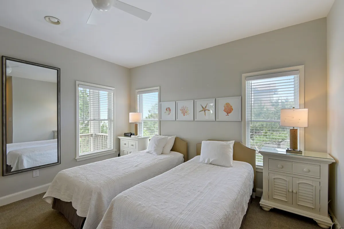 Another view of a twin bedroom, this one with modern framed artwork, a large mirror, and ambient bedside lamps. The sunlight streams in, enhancing the serene, welcoming mood—perfect for guests seeking comfort and ease.