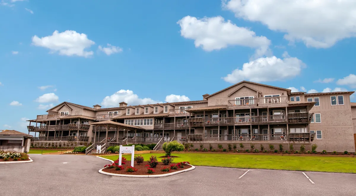 The welcoming facade of the resort's building is framed by balconies and a beautifully landscaped garden. People relax on the balconies and stroll through the grounds, enjoying the peaceful outdoor setting as the sun sets.